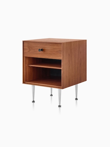 An angled view of a Nelson Thin Edge bedside table with a medium finish, black knob, and slim aluminum legs.  
