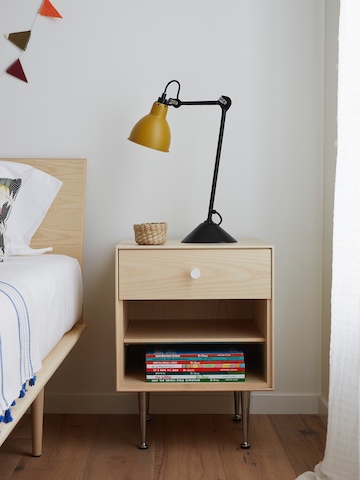 A lamp sits atop a Nelson Thin Edge bedside table positioned next to a bed.