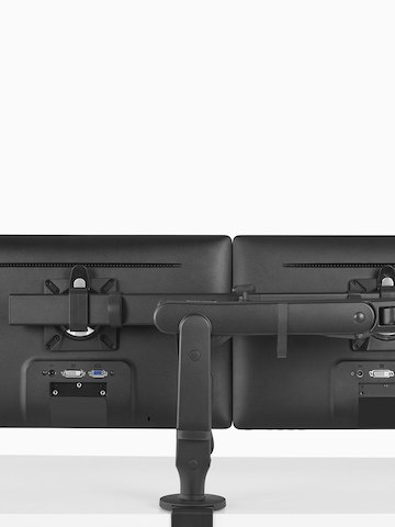 The back view of a black Ollin Monitor Arm supporting two monitors above a work surface. Select to go to the Ollin Dual product page.