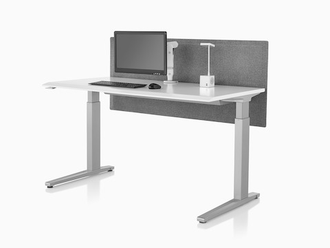 An Ollin Monitor Arm elevates a monitor off the surface of a sit-to-stand table that also supports a Cubert Personal Light.
