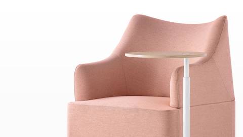 Close angled view of the sculptured back on a salmon Plex club chair paired with a height-adjustable work table. 