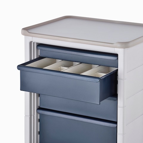 Detail of Procedure and Supply Cart in a soft white body and dark blue drawers with the top drawer open showing organizational subcontainers.