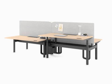 A cluster of four Ratio height-adjustable desks, positioned at seating and standing heights, attached side by side with framed, beige mounted privacy screens.