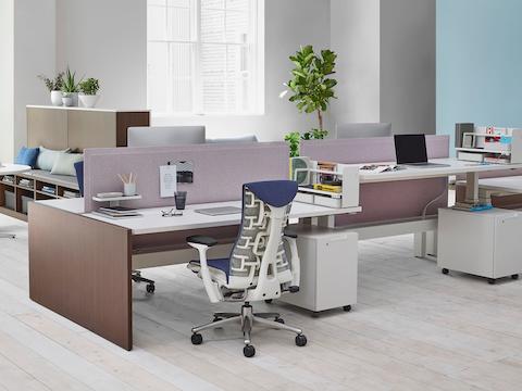 An office setting with a Renew Link standing desk system with blue Embody office chairs, dark wood supports, and purple fabric divider panel. 