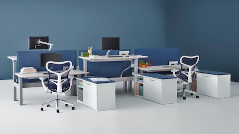A Renew Link standing desk system with blue Mirra 2 office chairs, blue fabric divider panels, and lower personal storage. Two of the six desks are raised to standing height.