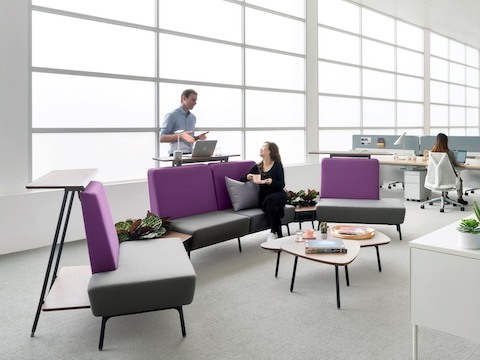 Dois colegas conversam em um espaço interativo, mobiliado com assentos Sabha roxo e cinza, apoiados em superfícies verticais.