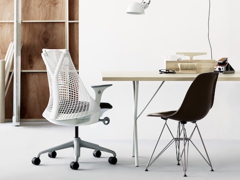 Pequeña oficina con una silla de oficina Sayl blanca, una silla de fibra de vidrio moldeada Eames negra con base de alambre y una tabla Nelson X-Leg.