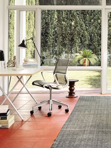 Black Setu office chair and a Nelson X-Leg Table in a glass-walled home office overlooking the outdoors.