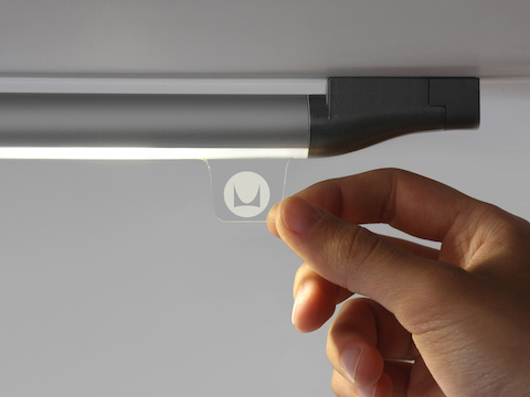Fingers grasp the tab of a Twist LED Task Light to control the illumination.