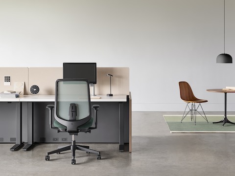 A black Verus chair with a black Motia Sit-to-Stand Table and Canvas Channel workstation with a Nelson Pedestal Table and Eames Molded Wood Side Chair in the background.