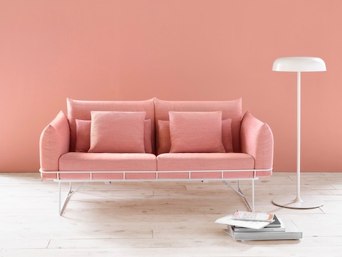 Two-cushion Wireframe Sofa in salmon with white frame, viewed from the front next to a floor lamp.