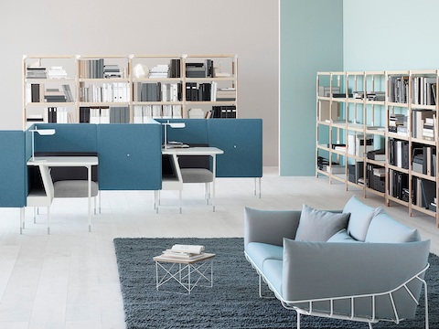 Light blue Wireframe Sofa with white frame, in a lounge space near two Public Office Landscape workstations with task lighting.