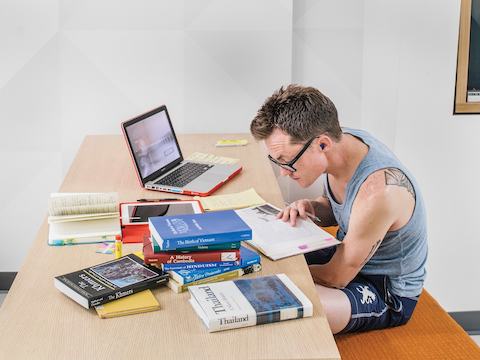 A student studies among a stack of books and a laptop. 