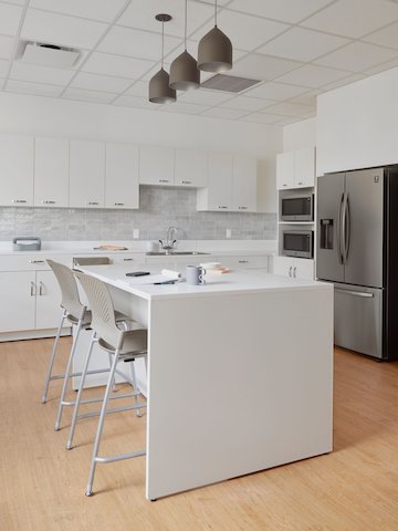 A staff break room with white laminate Mora casework along the backwall and an island of white Mora casework with two Caper stools in Cappuccino seat and back with silver legs.