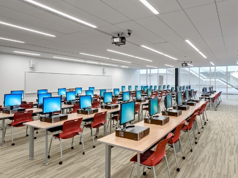 Computers sit atop several rows of desk and chairs within a university building. 