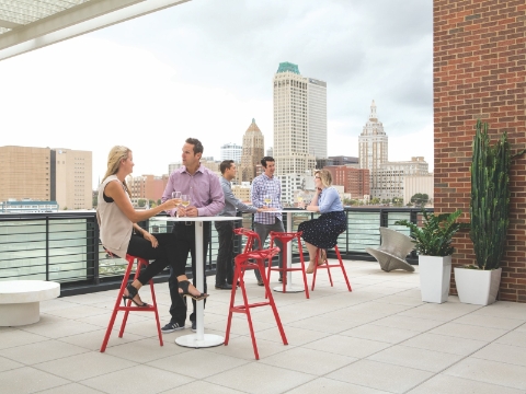 People talk outside on a patio overlooking a downtown area. 
