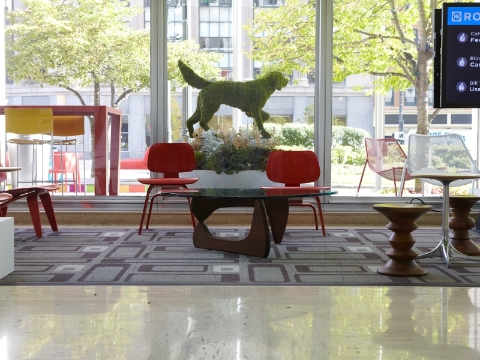 An office lobby displays Eames chairs and stools placed near windows. 