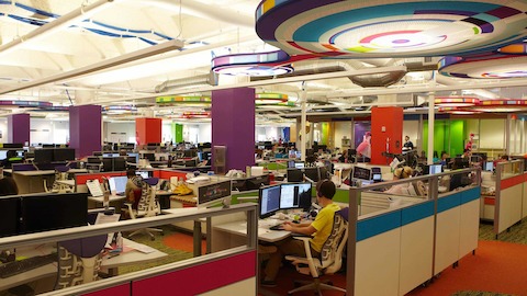 Employees go about thier work while sitting in colorful open workstations. 