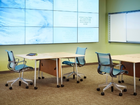 A college clasroom with tables and Setu chairs, and a video wall backdrop. 