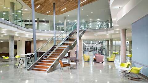 A large building lobby showcases a prominent staircase, with several lounge seating options.