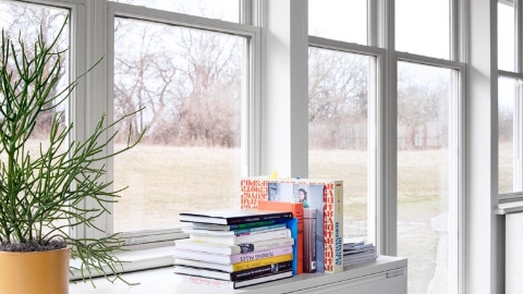 Books stacked atop a file cabinet near a wall of windows. Select to go to Herman Miller's white paper on nature-based design.