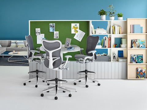 Three Mirra chairs sit at an empty table in front of shelving units. 