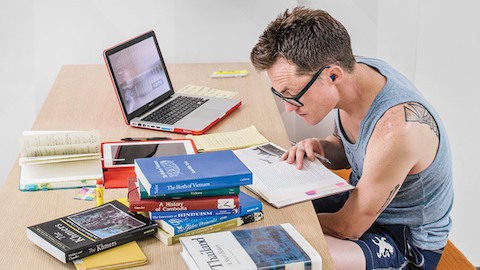 A student studies at a table piled with textbooks. Select to read a case study about California State University, Long Beach.