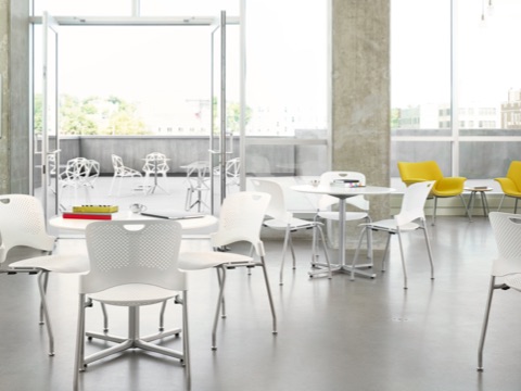 A student gathering space with floor-to-ceiling windows, white Caper Stacking Chairs, and yellow Swoop Lounge Chairs.