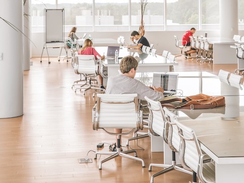Five college students, all sitting in white Eames Aluminum Group Chairs, work individually in a large study room. 