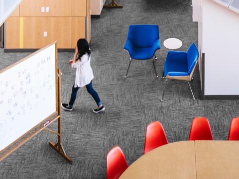 A college student walks through an interaction space featuring Swoop Plywood Lounge Chairs and Eames Molded Plastic Chairs. 