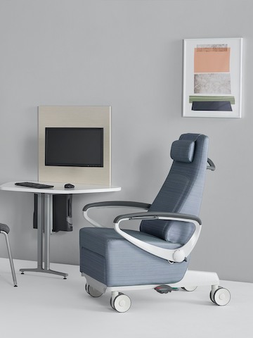 A light blue Ava patient chair with a Mora System peninsula on the side wall in an exam room setting.