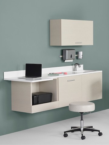 Mora System casework in an ash finish with a white solid surface top and sink. The casework is wall-hung and has an upper storage cabinet and lower storage cabinets, including a technology cabinet.