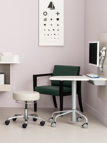 An exam room with Intent Solution wall unit holding a monitor on a Flo monitor arm and a mobile height adjustable table, with a Physician Stool, and a lounge chair.