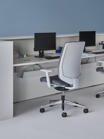 An interior view of a prefab Commend Nurses Station with a white work surface, white Corian transaction surfaces, Verus Chairs, and monitor stands.