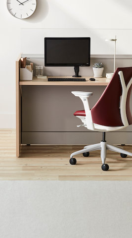 Nurse workstation of Ethospace in an ash veneer with light gray tiles, a monitor and monitor arm, and a Sayl chair in a maroon upholstery and white frame with gray base.