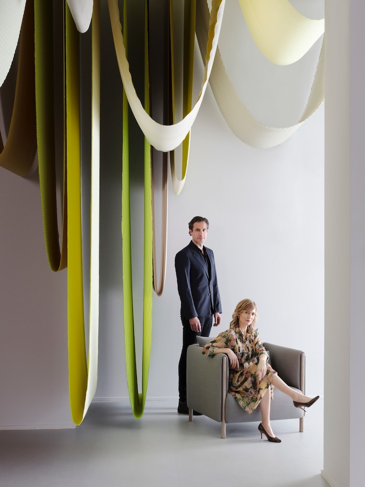 Designers Stefan Scholten, standing, and Carole Baijings, seated, next to hanging textiles.
