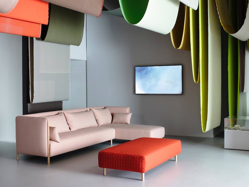 A pink ColourForm sectional and a red ColourForm ottoman beneath hanging textiles of various colors.