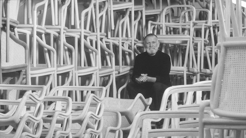 Designer Ward Bennett sits among dozens of stacked chairs. Select to go to an article about Bennett.