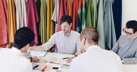 Four seated men review fabric samples. Select to go to an article about shaving company Harry's move to a Living Office.