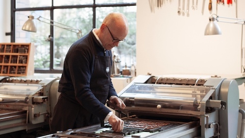 A man works with a printing press. Select to go to an article about the typeface used as Herman Miller's corporate font.