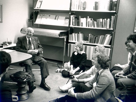 A black-and-white photo of Herman Miller founder D.J. De Pree chatting informally with a group of young people.