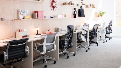 Six different models of Herman Miller office chairs pushed under a long desk. Select to find links to Herman Miller authorized retailers.