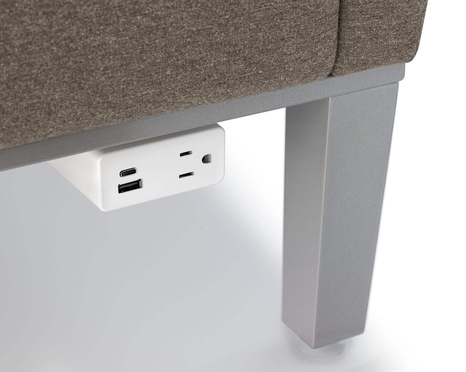 Zoomed-in shot of a white Herman Miller Mini Logic power outlet with USB-C port, USB-A port, and A/C power outlet mounted to the metal base of Brava Platform Lounge Chair.