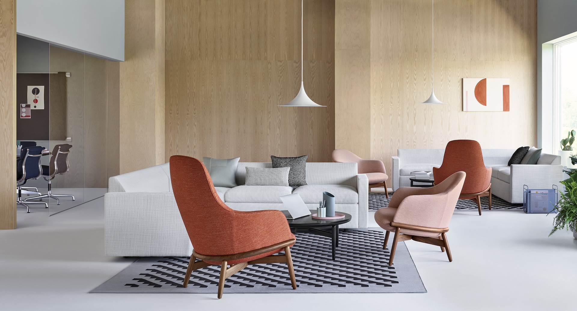A relaxed lounge setting with Reframe Lounge Chairs in the foreground. A Bevel Sofa sits on a patterned rug in the background.