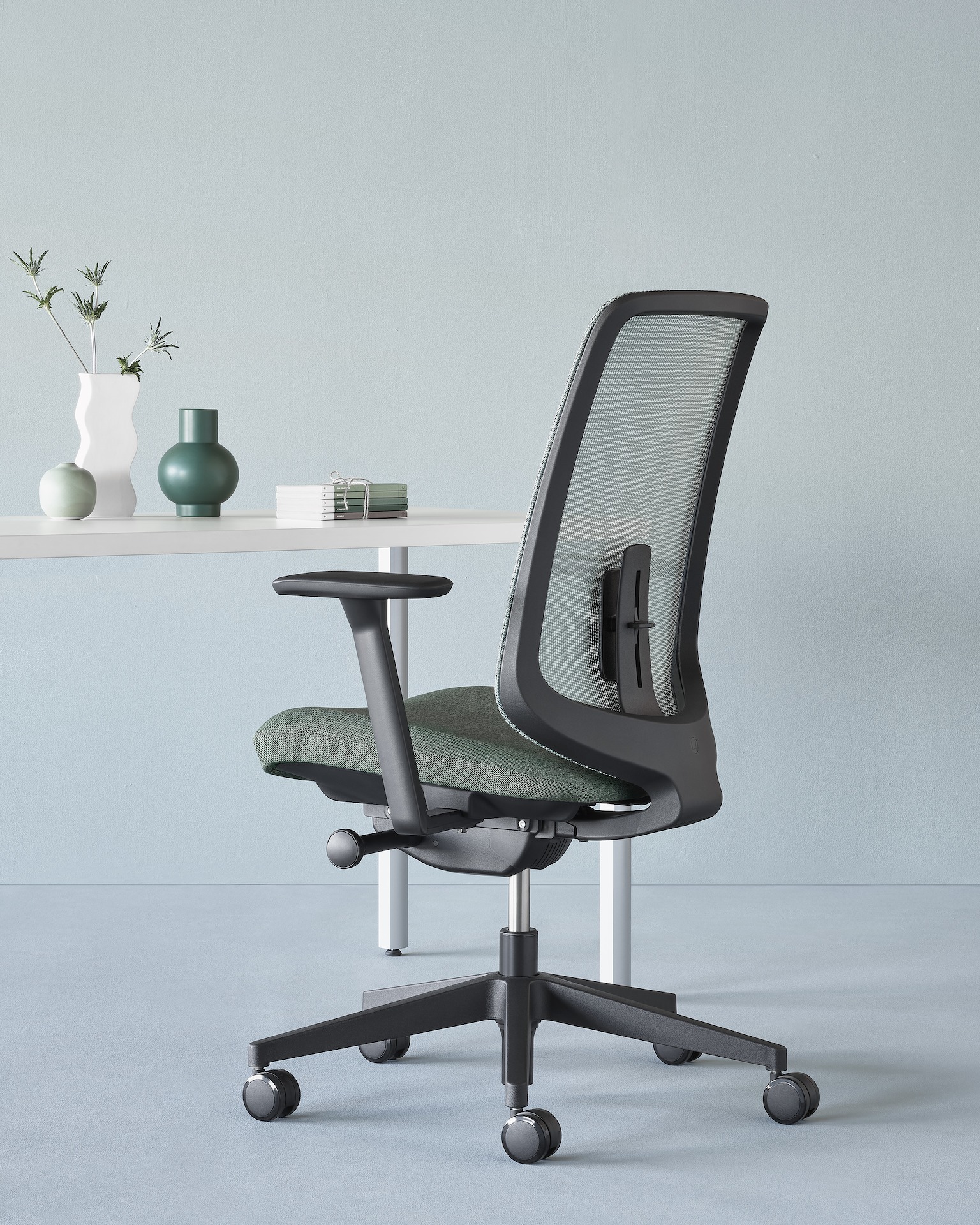 A black Verus Chair with adjustable lumbar support behind a white Everywhere Table. 