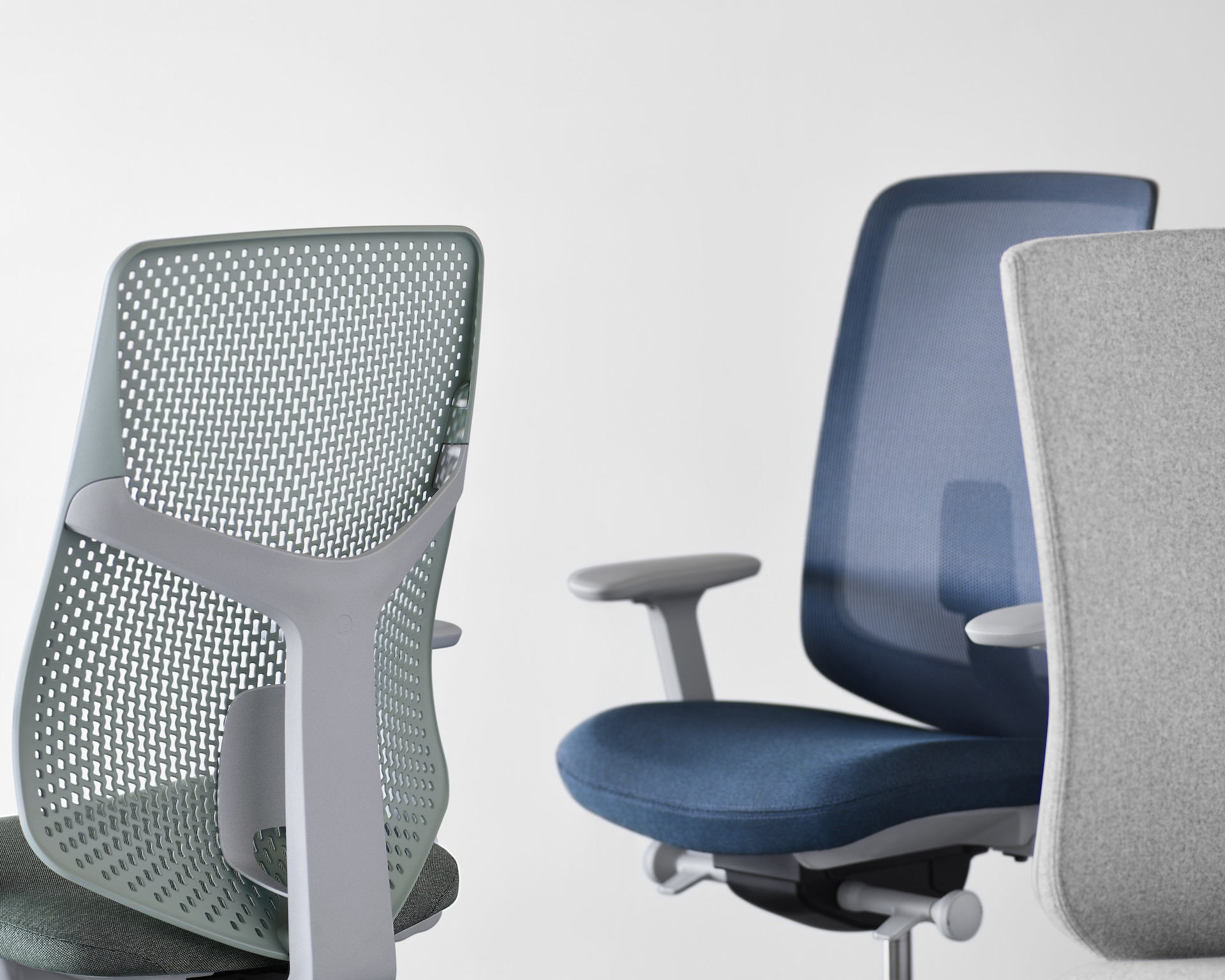 A Verus Chair with green Triflex back next to a blue suspension and grey upholstered version.