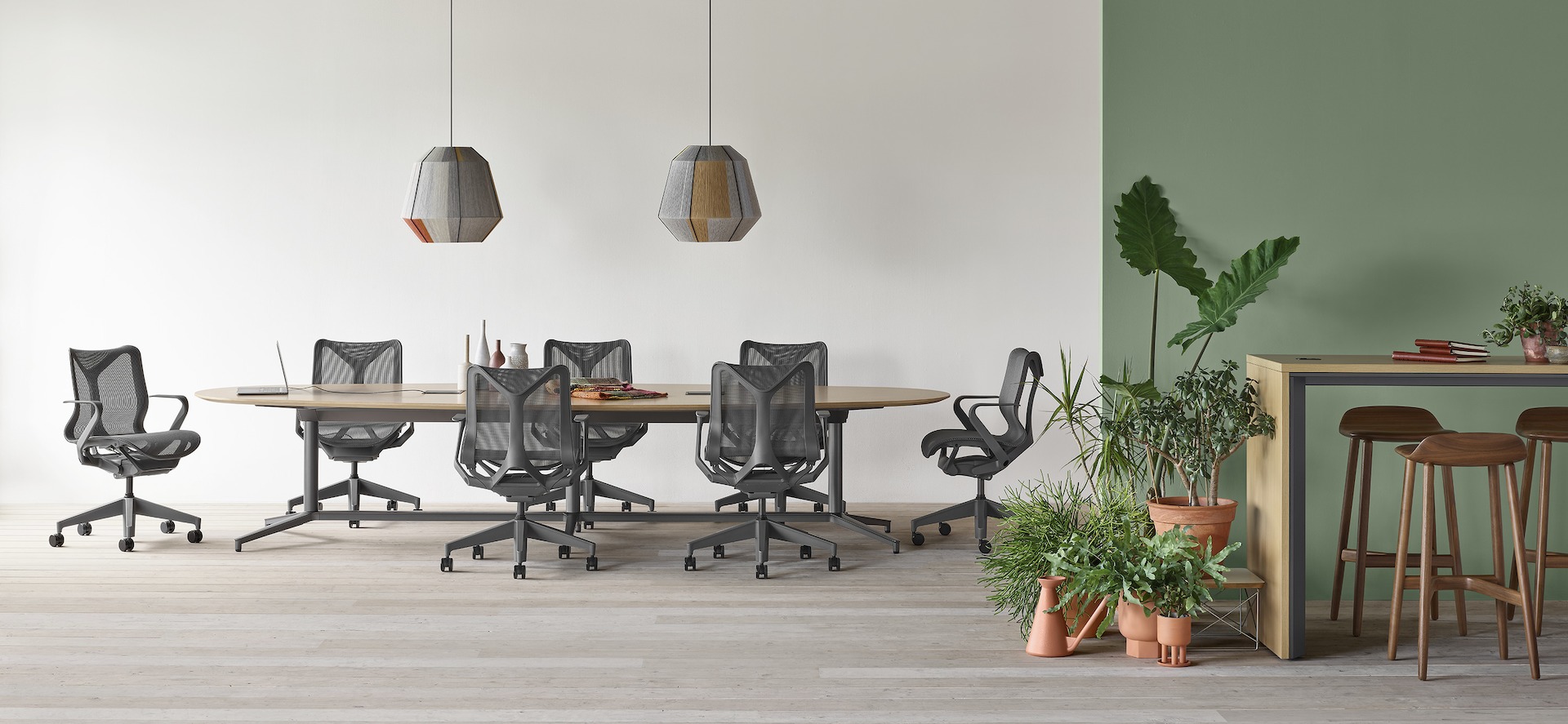 A Y base Headway conference table surrounded by seven Cosm chairs in an open conference space with a Headway communal table with Crosshatch stools nearby.