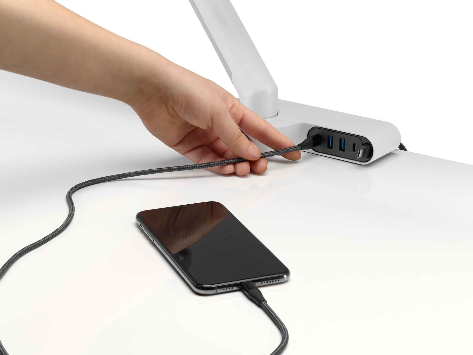 A person shown connecting a mobile phone charging cable to an Ondo Connectivity Module on a desk.