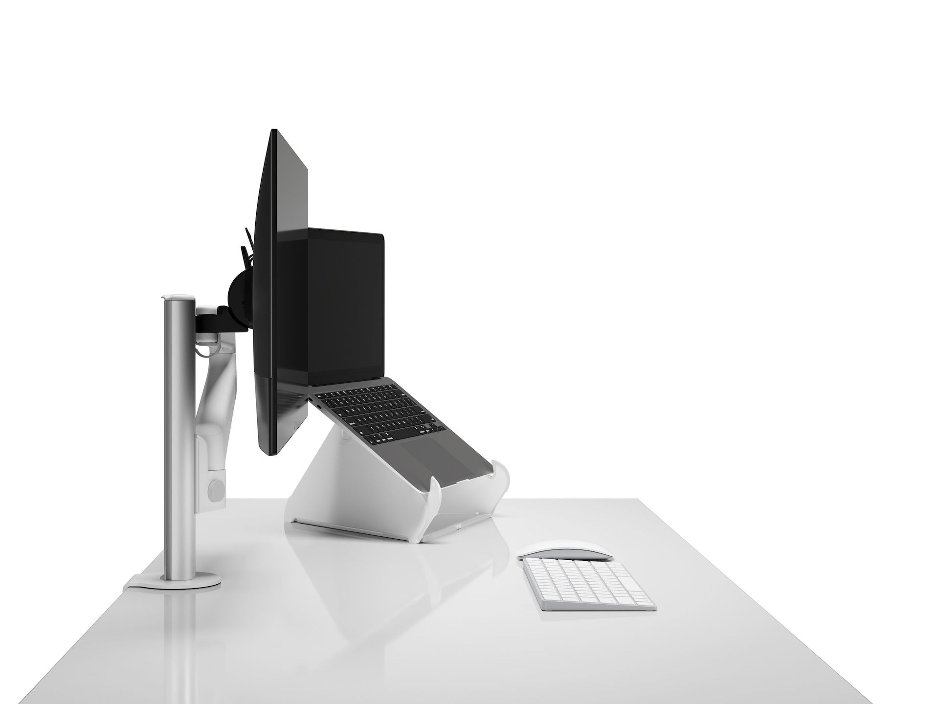 Side view of a monitor arm and screen next to open Laptop raised on an Oripura Laptop Stand on top of a worksurface with work tools.