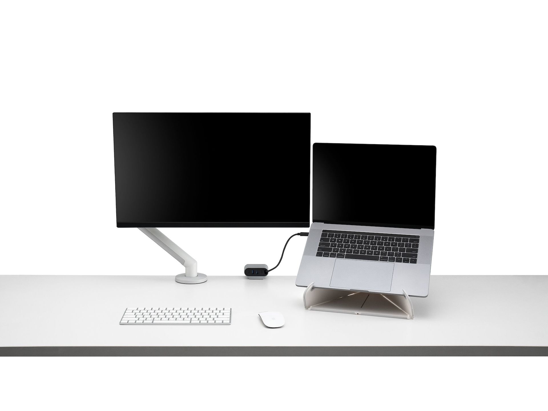 Front view of a screen attached to a Flo Monitor Arm integrated with an Ondo Work Surface Mount on a desk connected to a laptop with wireless keyboard and mouse that's supported by an Oripura laptop stand.